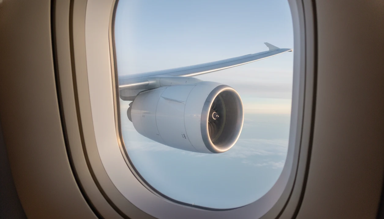 A passenger-window view of an airplane wing and engine climbing calmly above clouds after takeoff.